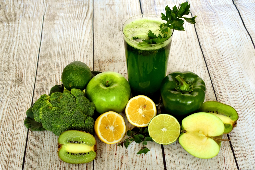 A green smoothie surrounded by fruits and vegetables.